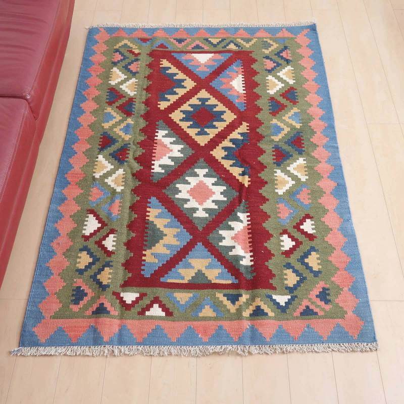 キリム・シラーズ/カシュガイ 183×122cm(KL-103)は、色とりどりの幾何学模様が魅力的なこの手織りウールのギャッベラグは、リビングルームの床にペルシャ絨毯専門店の通販商品として敷かれている。