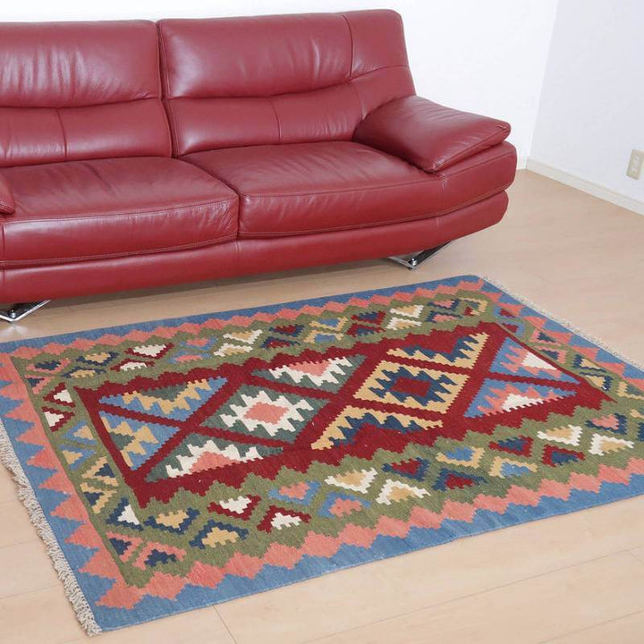 落ち着いた色合いの手織りギャッベラグが、赤いソファの前のリビングに温かみを添えている。
