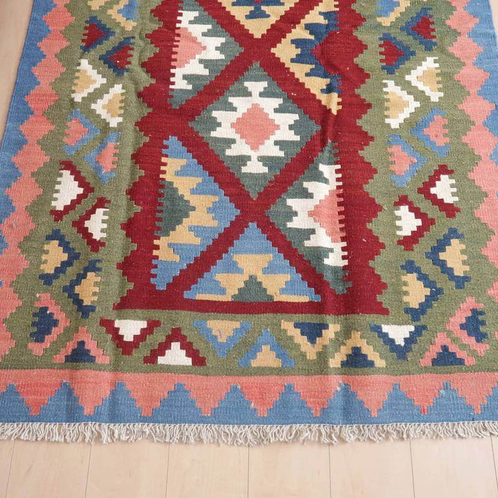 色鮮やかな幾何学模様が特徴の手織りギャッベラグが床に広がり、ペルシャ絨毯の専門店らしいウールの質感が際立っている。