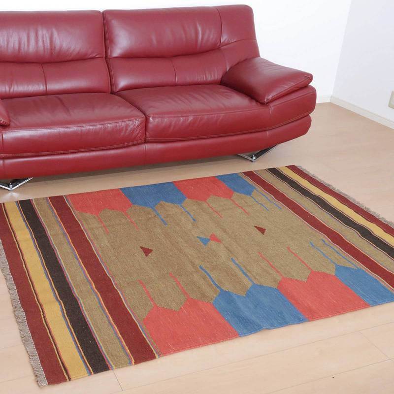 赤いソファの前に敷かれた、ペルシャ絨毯専門店の手織りギャッベラグは、ウール素材の暖かみある色彩がリビングに落ち着きを与えている。