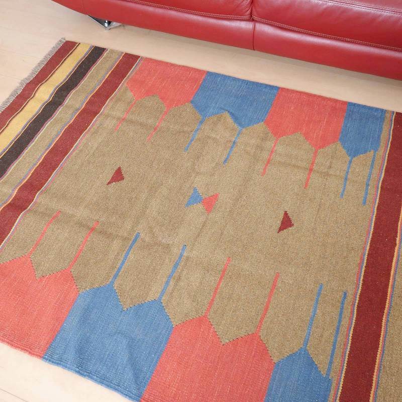 赤と青の幾何学模様が特徴的な手織りウールラグがリビングの床に敷かれ、温かみのあるペルシャ絨毯が専門店の通販で提供されています。