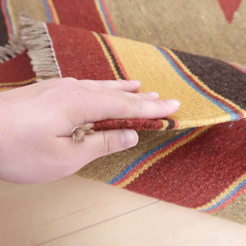 手でめくられたギャッベのラグは、温かみのある色調と丁寧に手織りされた厚みが際立ち、ウール素材の柔らかさが感じられます。