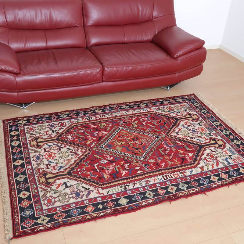 赤いソファの前に広がるペルシャ絨毯風のギャッベラグは、手織りのウール素材が醸し出すぬくもりと大胆な模様がリビングの床に映えている。