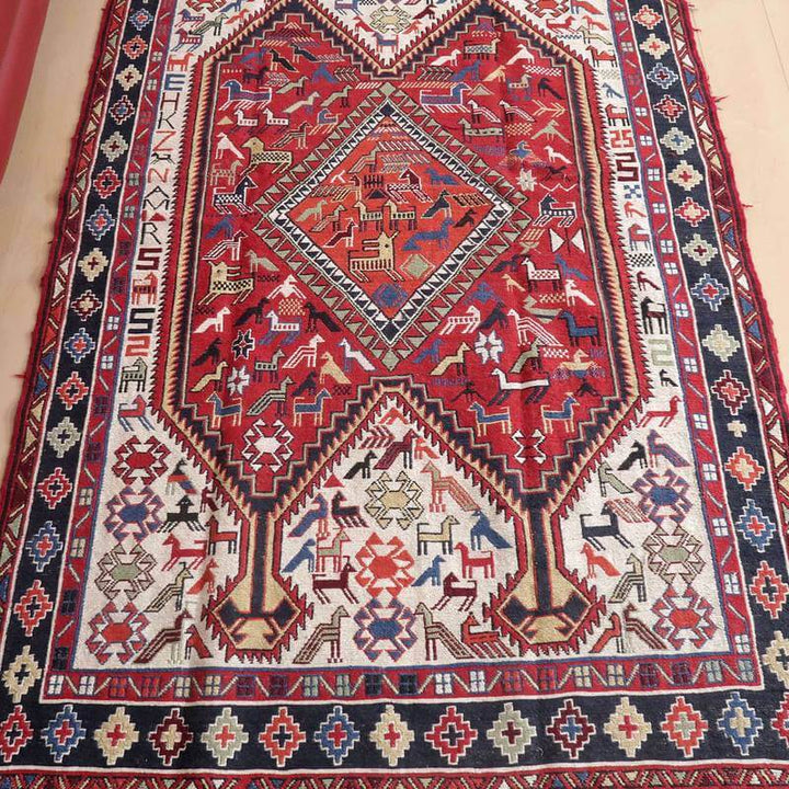 赤と青を基調とした複雑な幾何学模様が特徴のギャッベラグが、ウールの手織りで丁寧に仕上げられたペルシャ絨毯専門店の通販商品として床に敷かれている。