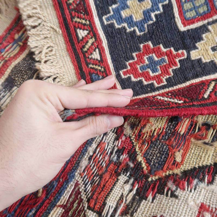 手に取られたギャッベのラグは、色鮮やかなペルシャ絨毯の模様が織り込まれており、手織りのウールの質感が際立っている。