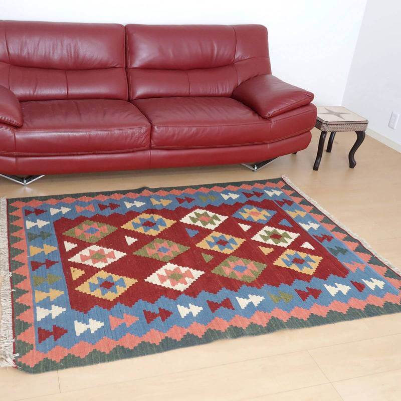 赤いソファの前に敷かれた鮮やかな幾何学模様のギャッベラグは、丁寧に手織りされたウール素材で、リビングルームに温かみを添えている。