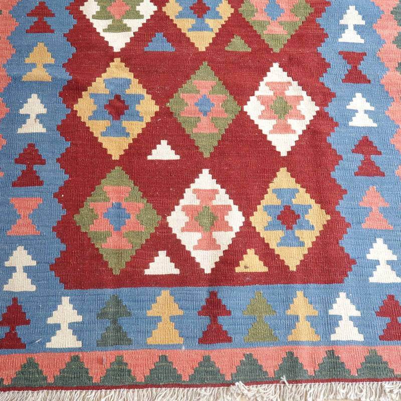 赤と青を基調にした幾何学模様の手織りギャッベラグが床に広がり、ウールの質感とペルシャ絨毯の伝統が際立っている。