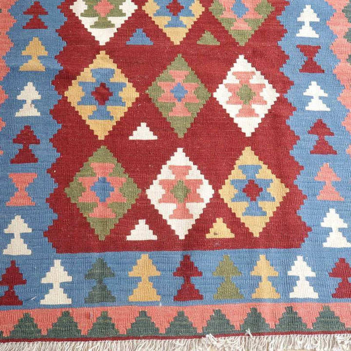 赤と青を基調にした幾何学模様の手織りギャッベラグが床に広がり、ウールの質感とペルシャ絨毯の伝統が際立っている。