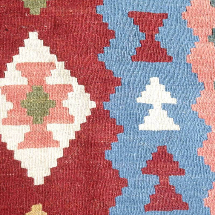 赤と青の幾何学模様が際立つペルシャ絨毯のギャッベラグが、手織りのウール素材で丁寧に織られた様子が見える。