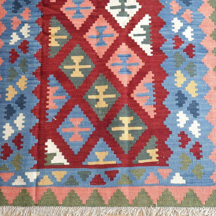 幾何学模様が美しい手織りのギャッベラグが広がり、鮮やかな赤と青のコントラストがペルシャ絨毯の伝統を感じさせる。