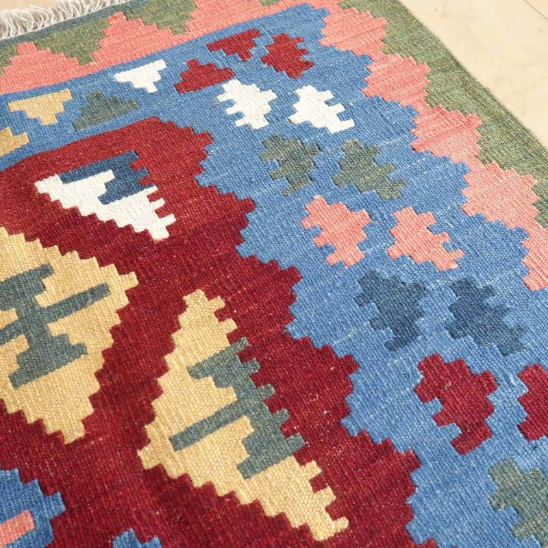 カラフルなペルシャ絨毯のギャッベラグが、手織りの温かみとウールの質感を感じさせる幾何学模様で床に敷かれている。