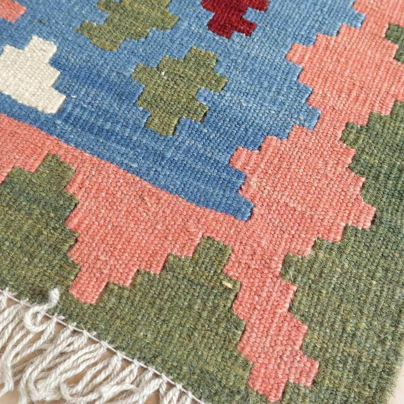 手織りのギャッベラグが持つ、青やピンク、緑の幾何学模様が織り込まれたウールの質感が際立っている。