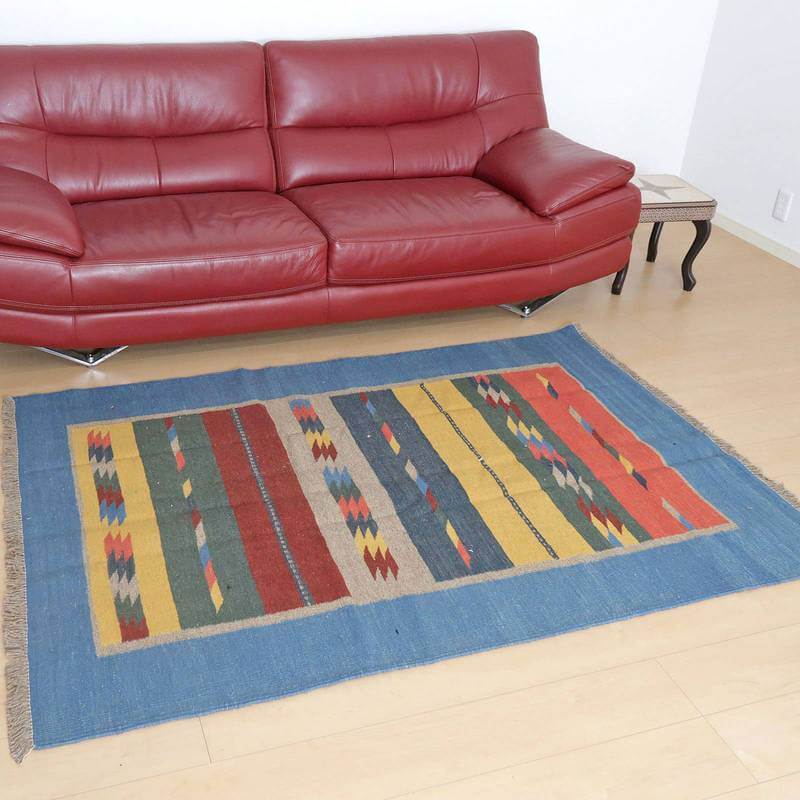 赤いソファの前に手織りのギャッベラグが敷かれており、鮮やかな幾何学模様とウールの温かみがリビングに彩りを添えている。