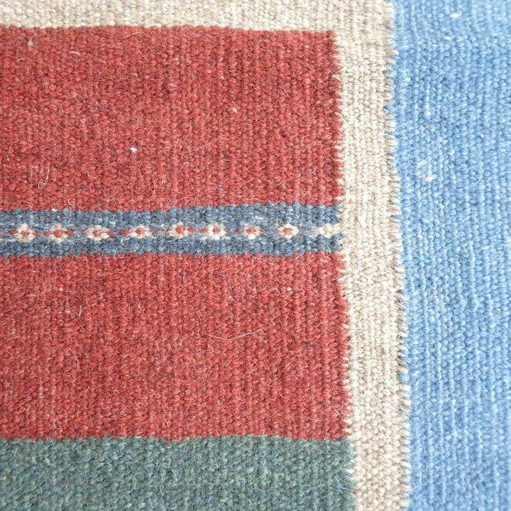 鮮やかな赤と青のストライプが織り込まれた手織りのギャッベラグが、ウールの温かみを感じさせながら際立っている。