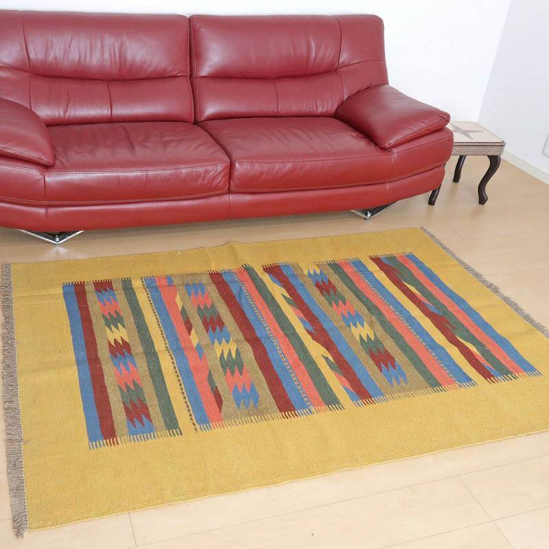 赤いソファの前に、ペルシャ絨毯を思わせる鮮やかな色彩の手織りギャッベラグが敷かれている。
