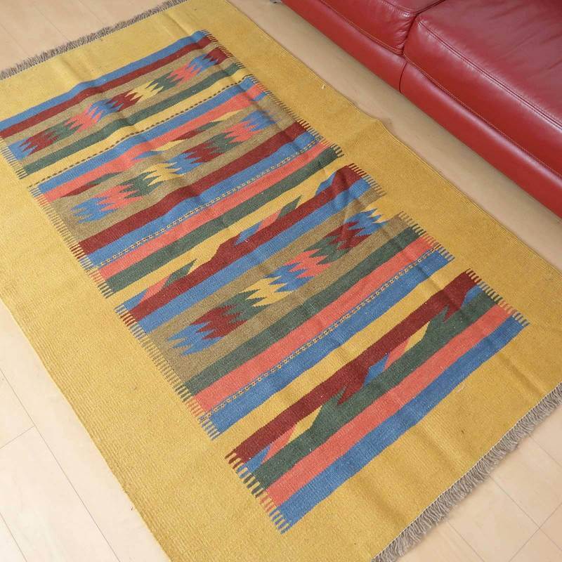 カラフルなストライプ模様が特徴の手織りウールラグがリビングの床に広がり、温かみのある色合いがペルシャ絨毯専門店の通販で人気を集めています。