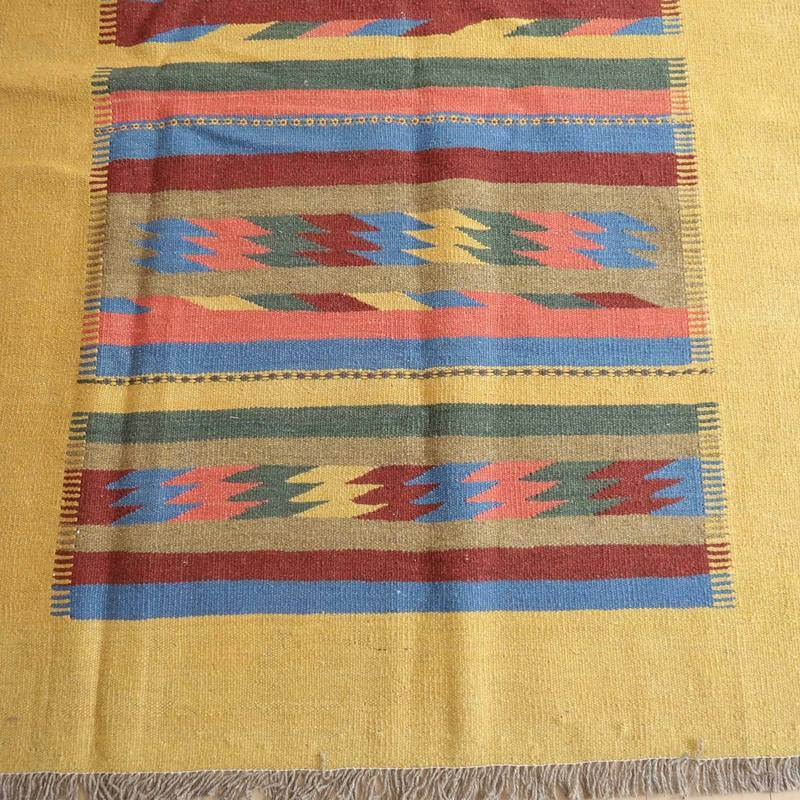 カラフルな模様と温かみのある色彩が特徴の手織りギャッベラグが床に広がり、ウール素材の柔らかさが際立っている。