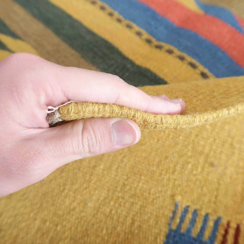 手織りのギャッベラグの厚みを指でつまみ、ウールの温かみある質感と色鮮やかなペルシャ絨毯の模様が際立っている。