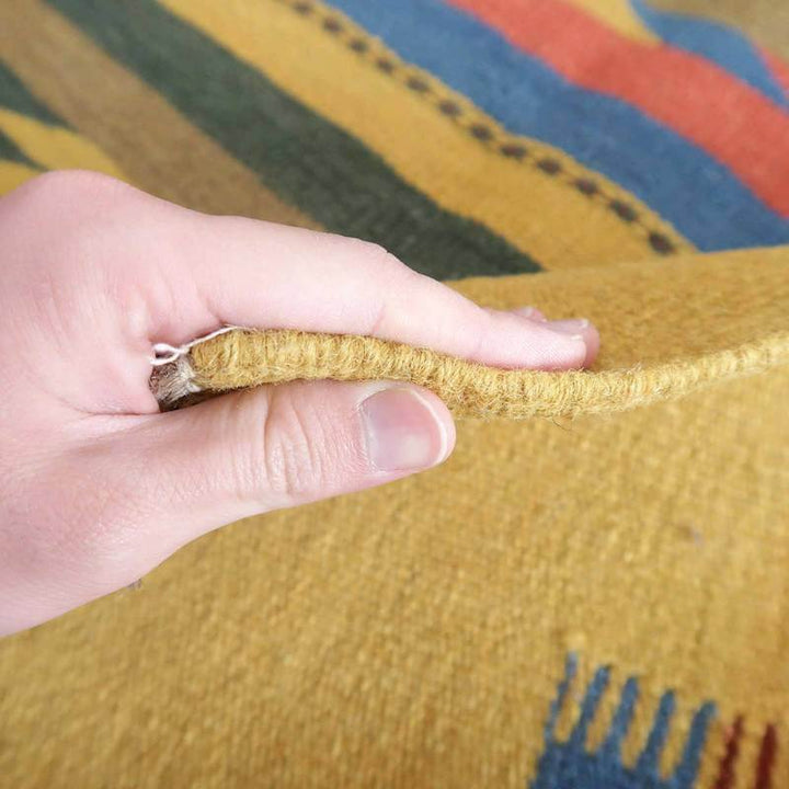 手織りのギャッベラグの厚みを指でつまみ、ウールの温かみある質感と色鮮やかなペルシャ絨毯の模様が際立っている。