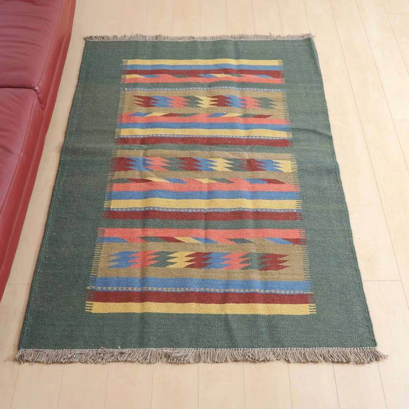 キリム・シラーズ/カシュガイ 186×124cm(KL-408)は、緑を基調にカラフルな模様が施された手織りのウールラグがリビングの床に敷かれ、ペルシャ絨毯の専門店ならではのぬくもりが感じられる。