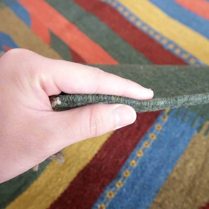 手織りのギャッベラグを指でめくり、その厚みとウールの柔らかさを感じる様子が見える。