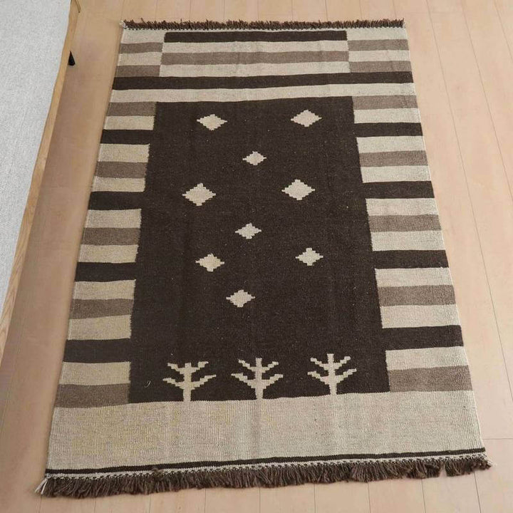 キリム・シラーズ/カシュガイ 183×125cm(KL-864)は、モダンな幾何学模様が特徴のブラウンとベージュのギャッベラグが、手織りの温かみを感じさせながら床に敷かれている。