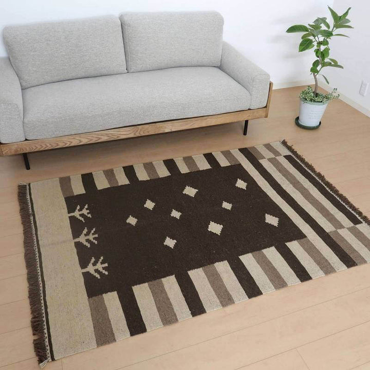 グレーのソファ前に落ち着いた茶色とクリーム色の手織りギャッベラグが敷かれ、モダンなリビングにぬくもりを添えている。