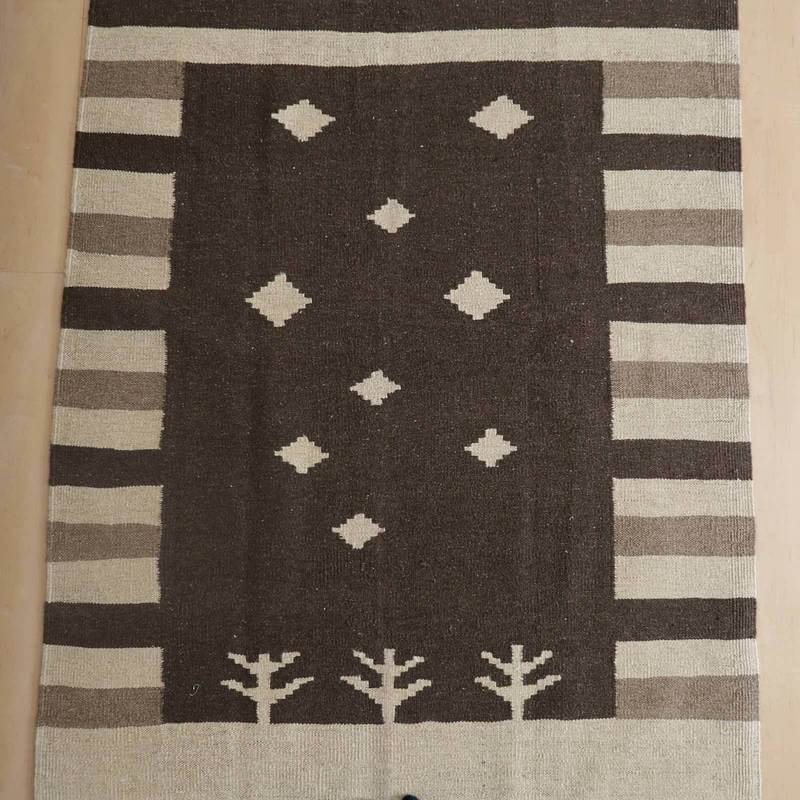 落ち着いたブラウンとベージュのコントラストが美しい手織りのギャッベラグは、ウールの温もりが感じられるペルシャ絨毯の専門店通販商品として床に敷かれている。