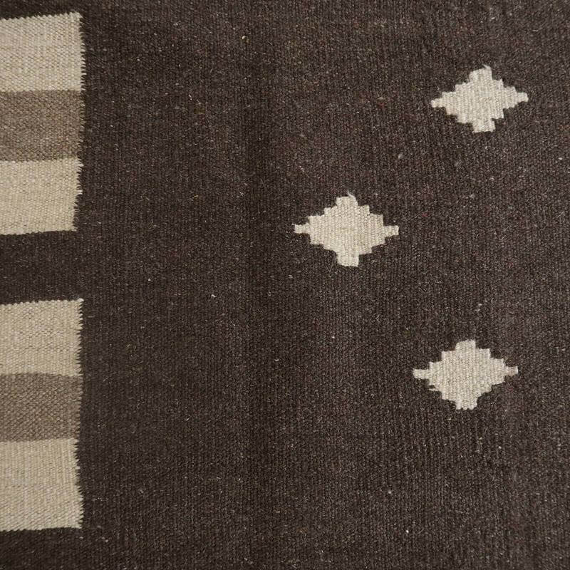 手織りのギャッベラグが、深いブラウンに幾何学模様を施し、ウール素材の柔らかさとペルシャ絨毯の伝統が調和している。