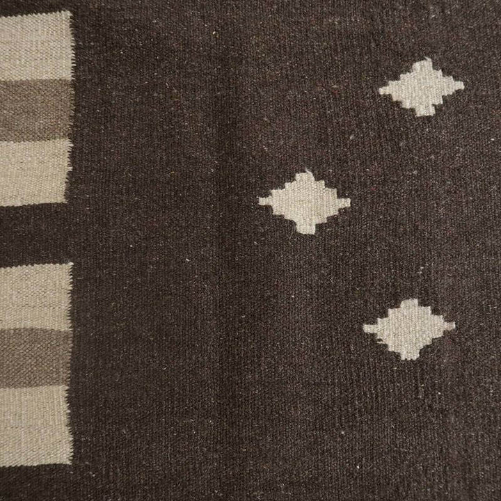 手織りのギャッベラグが、深いブラウンに幾何学模様を施し、ウール素材の柔らかさとペルシャ絨毯の伝統が調和している。