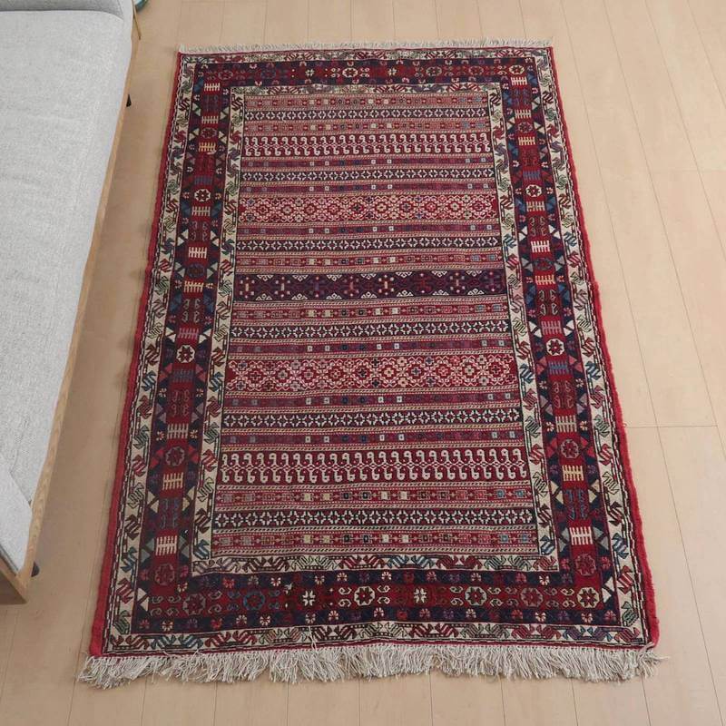 キリム・アゼルバイジャン 208×128cm(KL-974)は、手織りのウールで作られたペルシャ絨毯が床に広がり、深みのある赤と複雑な模様が専門店のリビングに優雅さを添えている。