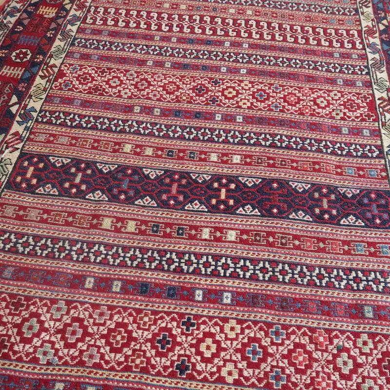 赤と青の幾何学模様が美しい手織りのギャッベラグが、ペルシャ絨毯の専門店で通販されており、繊細なウールの織り目が際立っている。