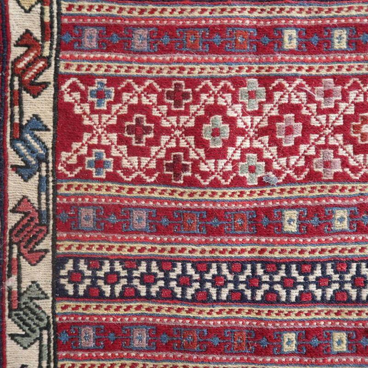 赤と青の幾何学模様が美しいペルシャ絨毯の手織りギャッベラグが、丁寧に紡がれたウールの織り目を際立たせています。