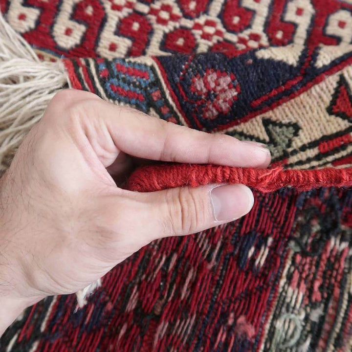 手織りのウールで丁寧に作られたペルシャ絨毯の縁を持ち上げ、厚みと織りの密度を確認する様子が見える。