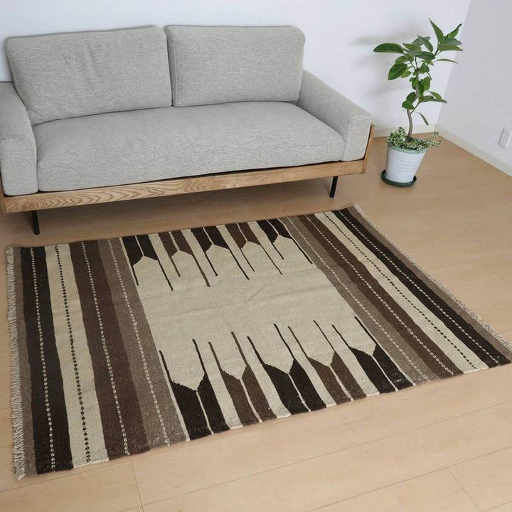 落ち着いたベージュとブラウンのストライプ模様が美しい手織りのウール製ギャッベラグが、シンプルなソファの前に敷かれている。