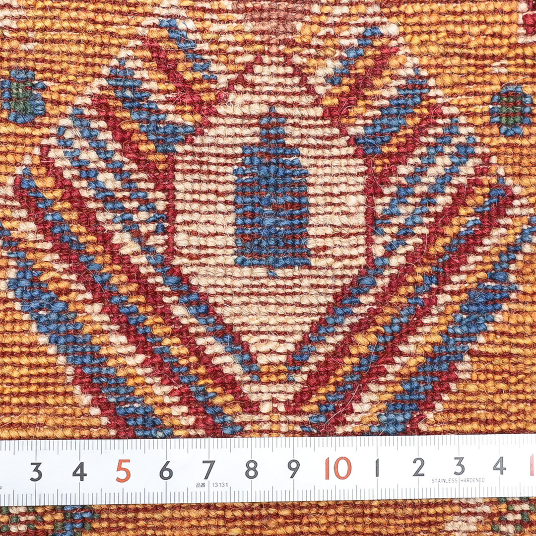 青と赤の幾何学模様が織り込まれた布の拡大写真、下にメジャーが置かれている