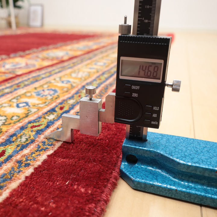 デジタルノギスで赤い絨毯の厚みを測っている様子のクローズアップ写真
