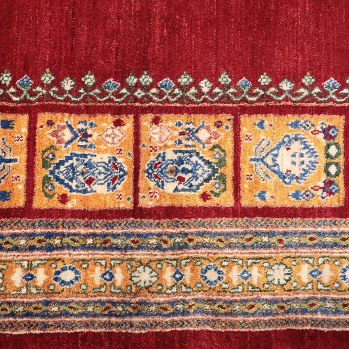 赤い背景に黄色と青の伝統的な模様が並ぶ織物の一部を示す画像。