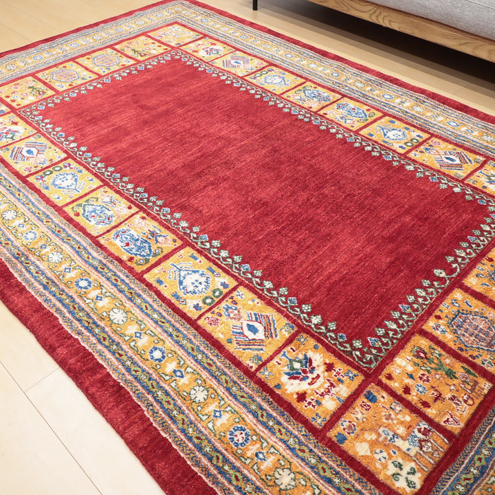 赤い中央部分と多彩な幾何学模様が並ぶ縁取りが特徴的な伝統的なデザインの敷物。