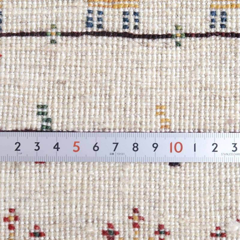 手織りのギャッベラグの織り目が精緻に見え、ウール特有の温かみを感じる一枚に定規が添えられている。