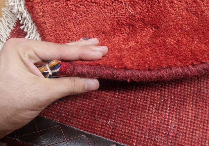 Rug in red tones — edge lifted to show the pile and thickness