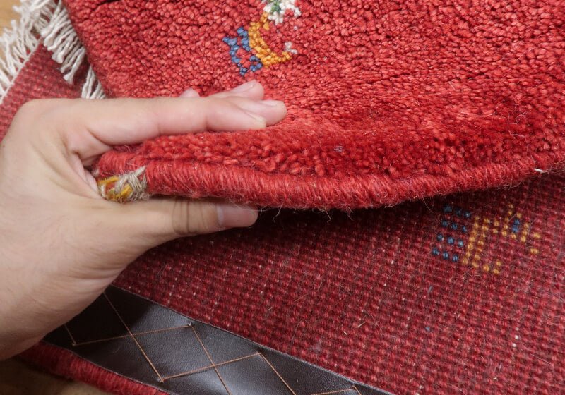 Rug in red tones — edge lifted to show the pile and thickness