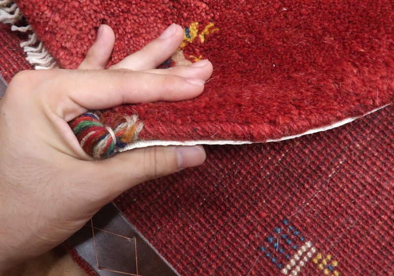 Rug in red tones — edge lifted to show the pile and thickness