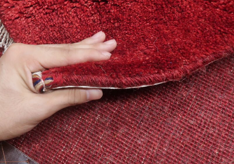 手織りのギャッベラグを手でめくり、その厚みとウールの温かみのある質感が際立っている様子が見える。