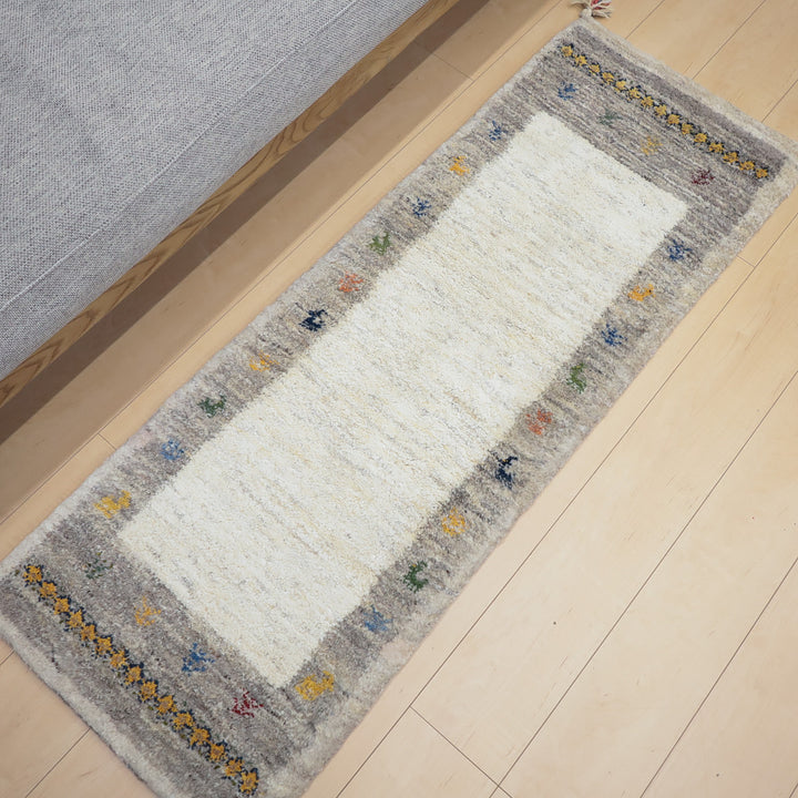 淡いグレーの縁に小さなカラフルな模様が並ぶ長方形の白いラグマットが床に敷かれている。