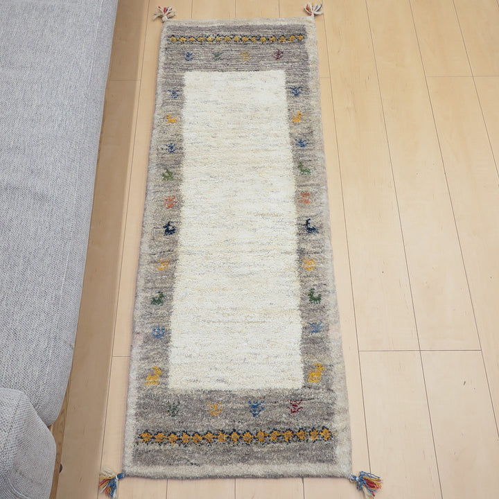 淡いグレーの縁にカラフルな模様が入った白い長方形の織物が木製床の上に置かれている。