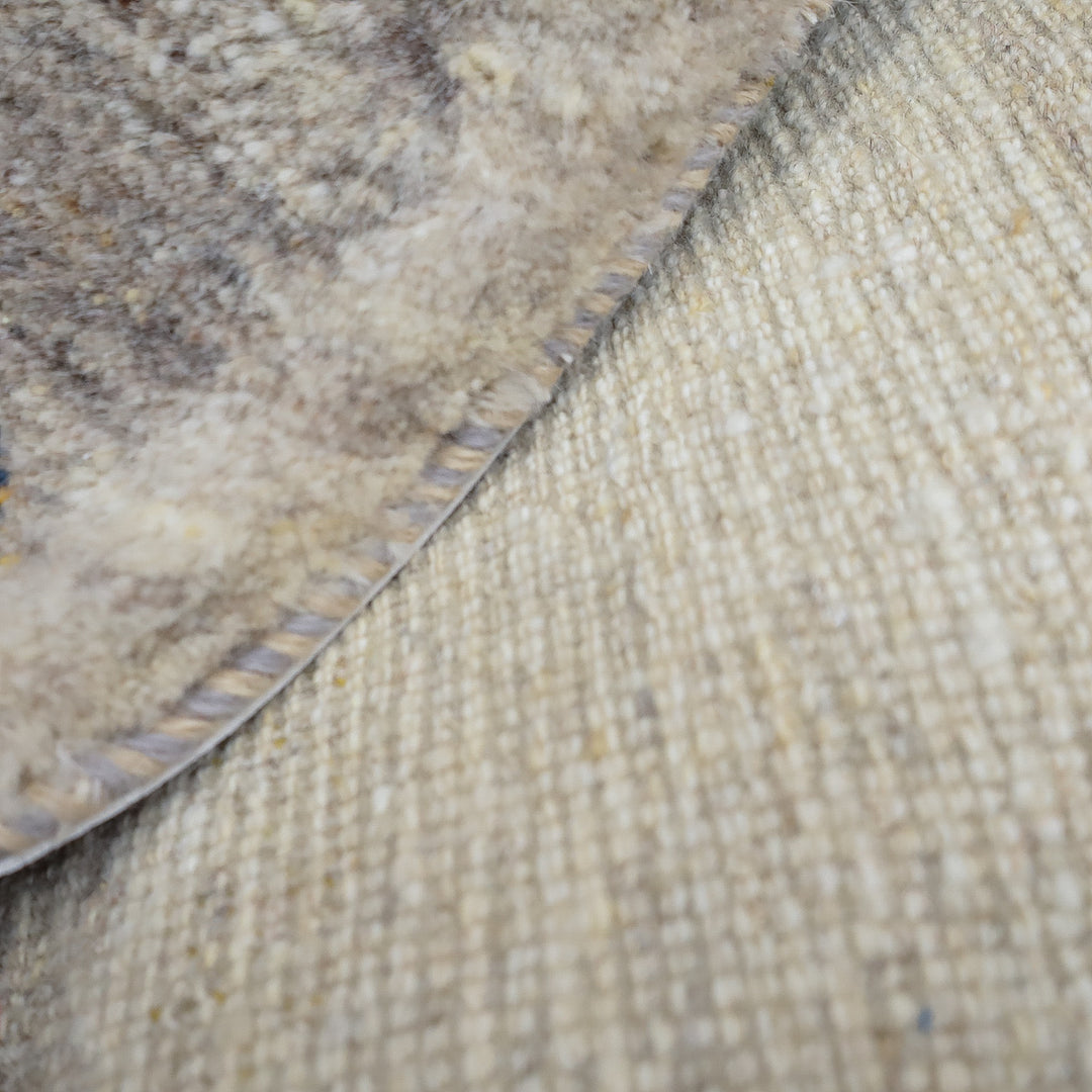 織り目が細かいベージュ色の生地の上に、縁取りのある毛足の長いグレー系ラグの一部が重なっている様子。