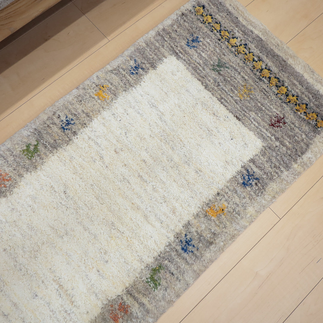 淡いグレーの縁に小さなカラフルな模様が並ぶ、中央がクリーム色の長方形のラグマット。