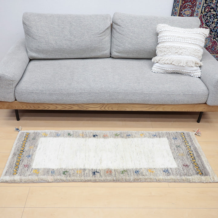 グレーのソファと白い装飾クッションの前に置かれたデザイン入りの長方形ラグ
