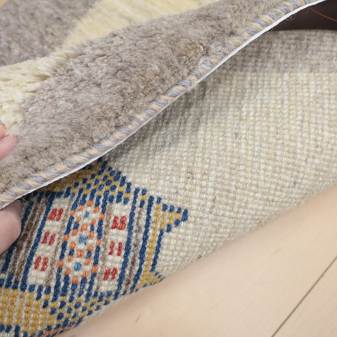 手でめくった毛足の長いラグの裏側に伝統的な柄が見えるクローズアップ写真